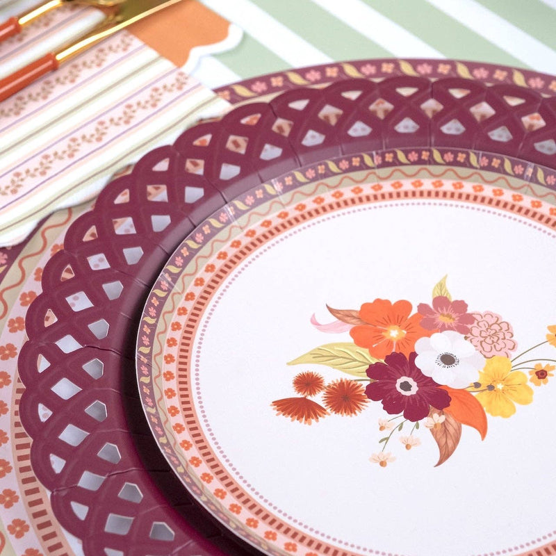 Styled fall place setting showing the burgundy plate layered under a white floral salad plate with a burgundy napkin and autumn florals.