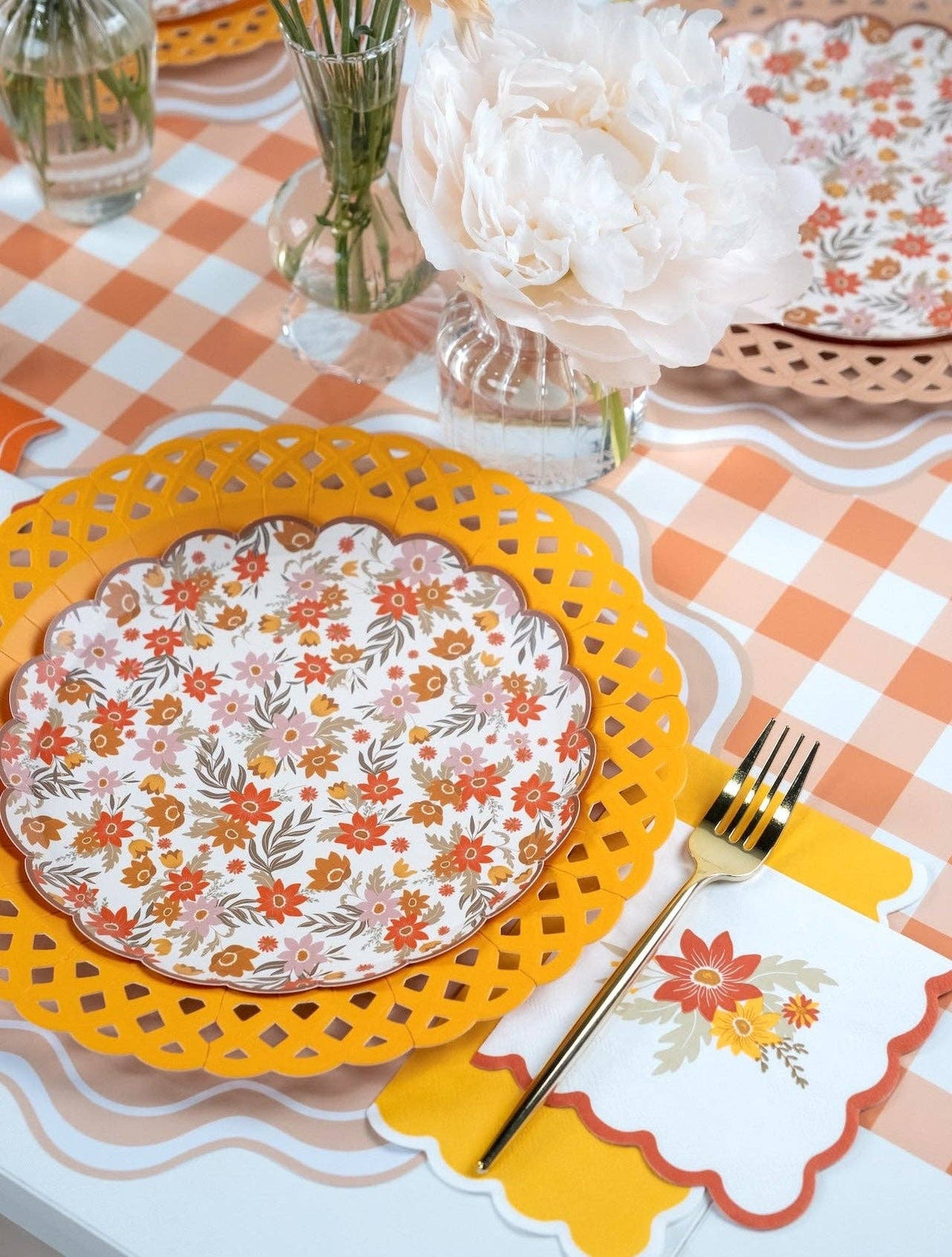 Angled place setting with a floral dessert plate on a marigold charger and white peonies in bud vases