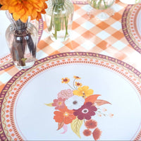 Styled fall place setting showing the floral placemat as the base under a white floral plate, with a black cat figure and gingham runner.