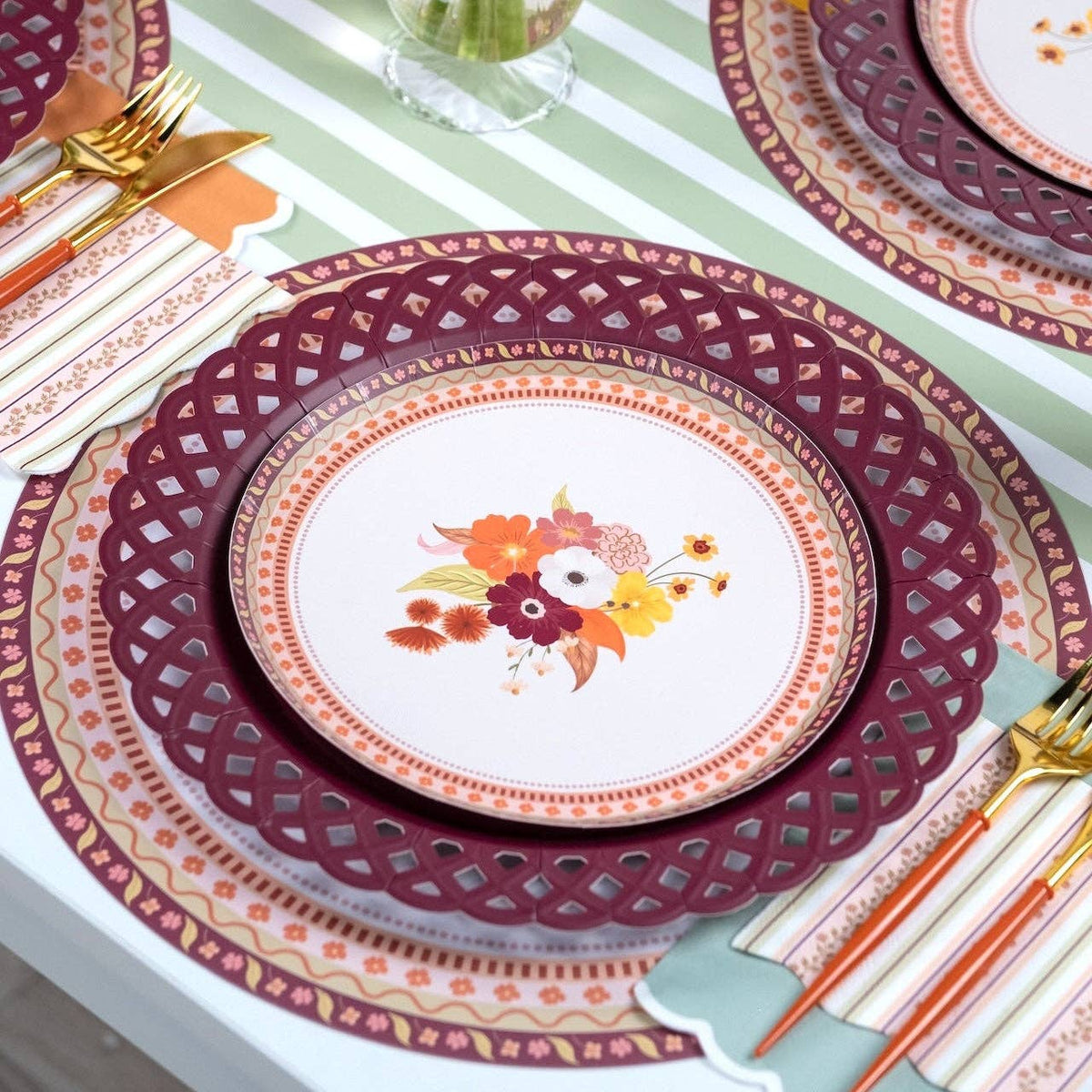 Overhead fall place setting showing the floral dessert plate on the burgundy plate with gold flatware on a green-striped runner.