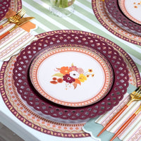 Overhead fall place setting showing the floral dessert plate on the burgundy plate with gold flatware on a green-striped runner.