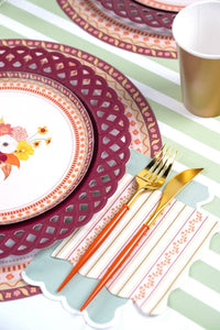 Fall place setting with a floral plate layered on the burgundy plate, gold flatware, and the striped harvest napkin.