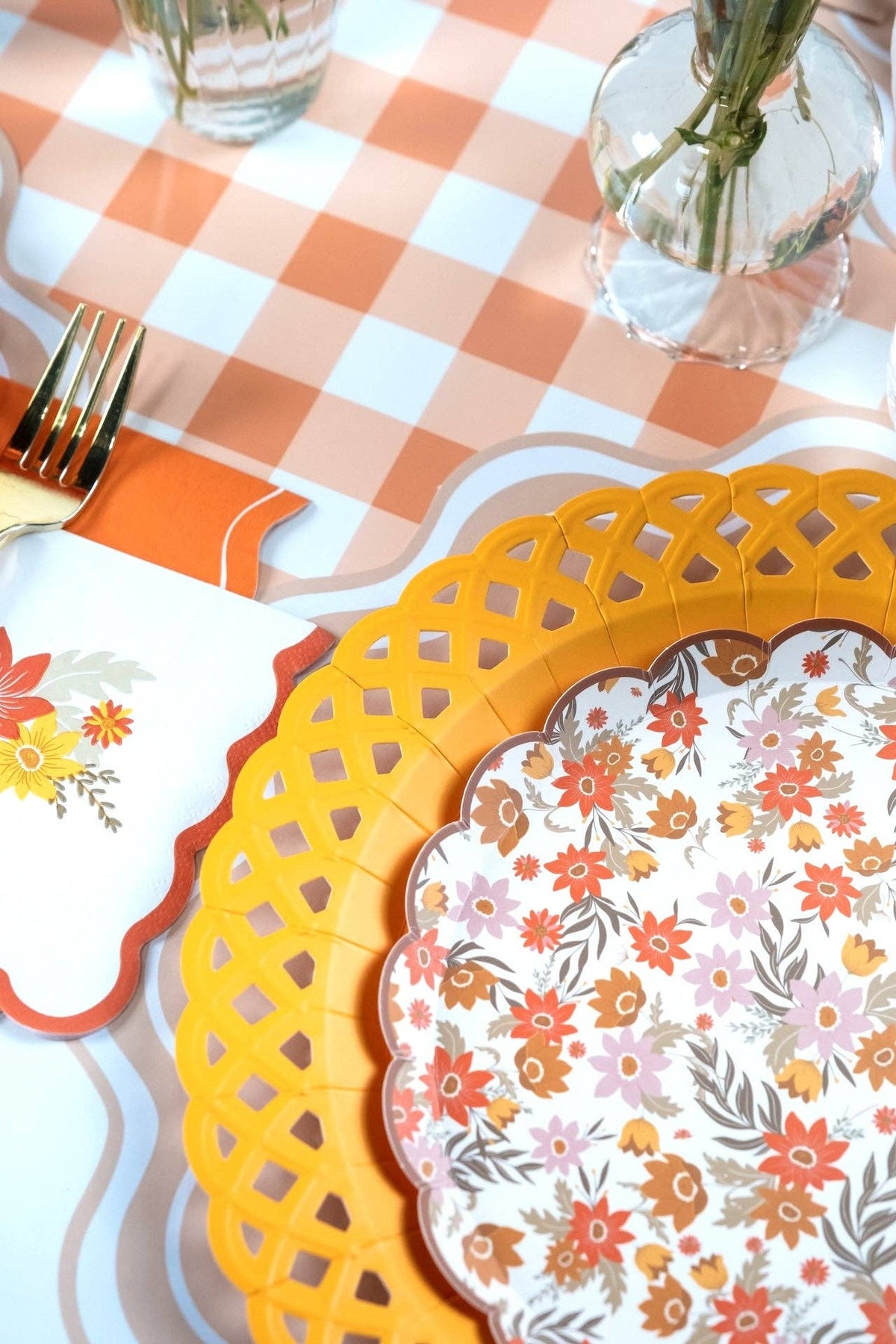 Fall place setting showing a floral plate on the yellow basketweave charger with gold flatware and a gingham runner.