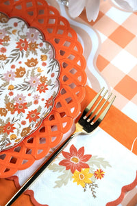 Fall place setting close-up showing the orange lattice charger, floral plate, gold flatware, and the orange scalloped guest towel.