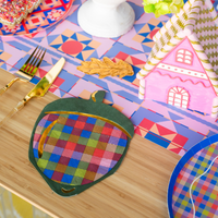 Overhead fall place setting showing the plaid acorn napkin beside a plate with a gingerbread house and colorful autumn décor on a plaid runner.