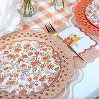 Styled fall place setting showing the tan napkin with floral plates on a scalloped charger over a gingham runner.