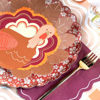 Close-up fall place setting showing a turkey scalloped plate on the burgundy basketweave plate with orange florals.