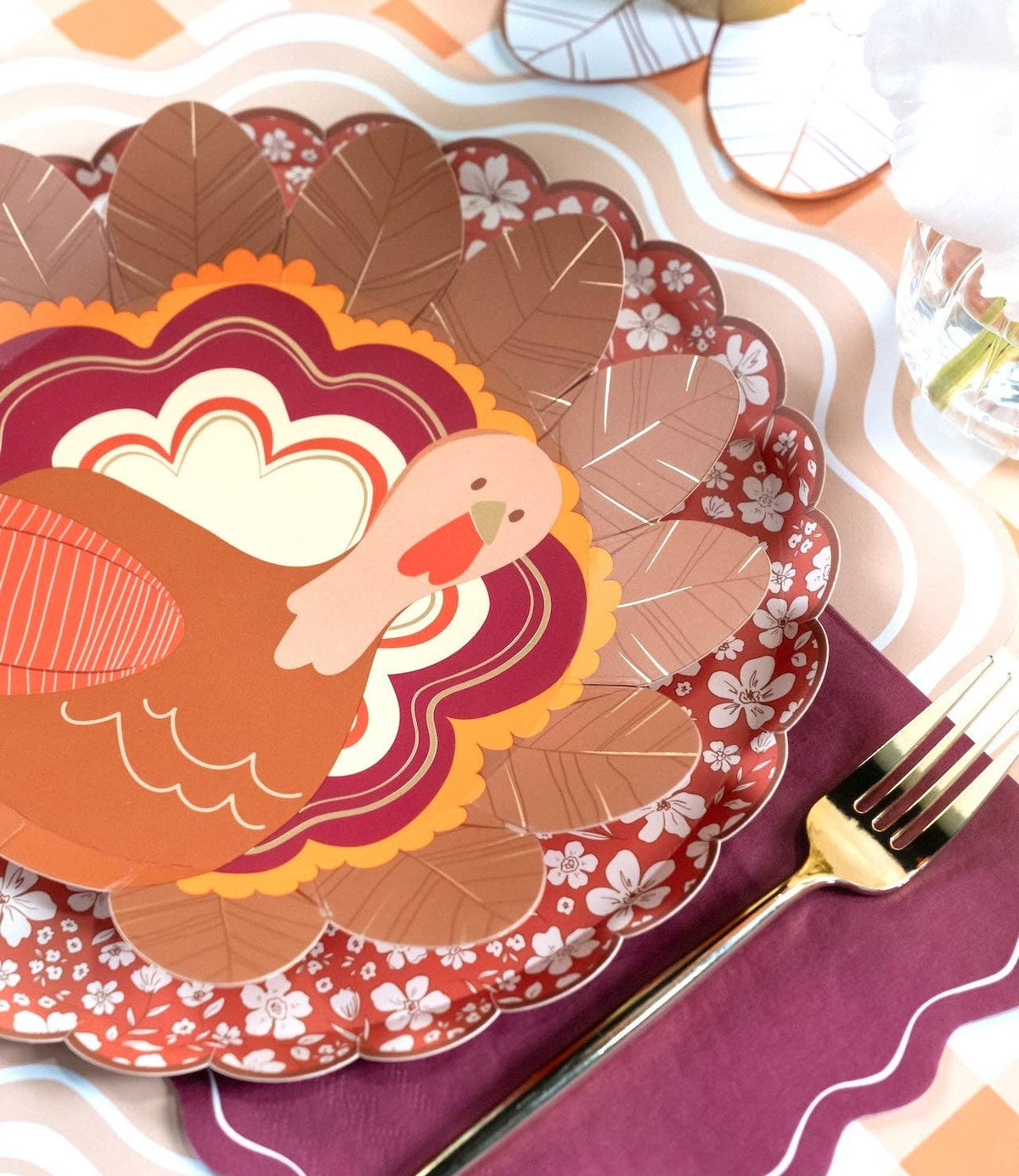 Fall place setting showing the turkey plate on a burgundy floral plate with a burgundy napkin and gold flatware.