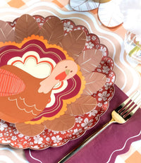 Fall place setting showing the turkey plate on a burgundy floral plate with a burgundy napkin and gold flatware.