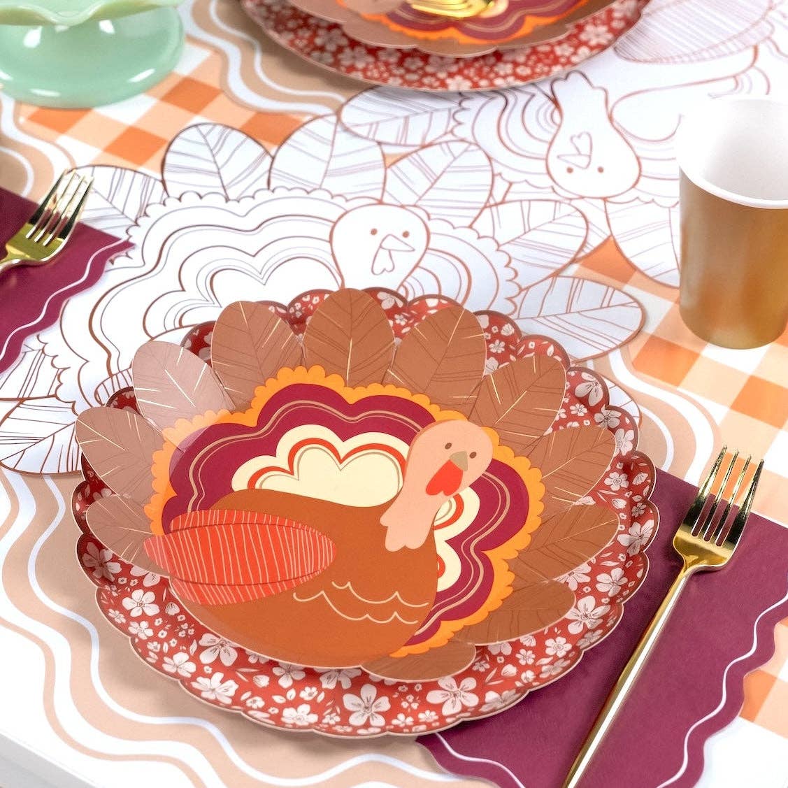 Fall place setting with a turkey plate layered on the burgundy plate, gold flatware, and the burgundy napkin.