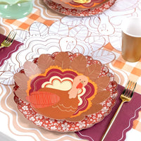 Fall place setting with a turkey plate layered on the burgundy plate, gold flatware, and the burgundy napkin.