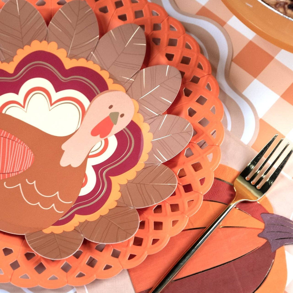 Styled fall place setting showing the turkey plate layered on an orange lattice charger with a burgundy napkin and gingham runner.