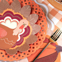 Styled fall place setting showing the turkey plate layered on an orange lattice charger with a burgundy napkin and gingham runner.