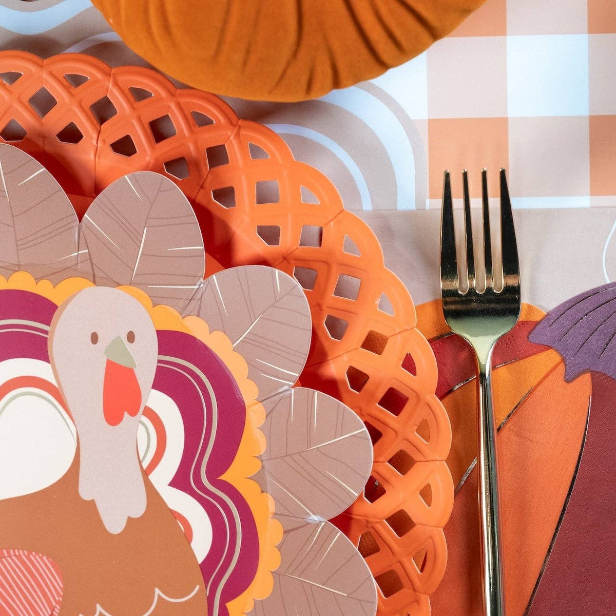 Close-up fall place setting showing the turkey plate on an orange lattice charger with a burgundy napkin and gold fork.