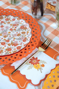 Floral dessert plate layered on an orange lattice charger with a gold fork and scalloped napkins