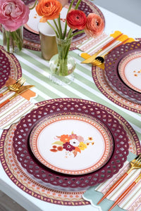 Overhead fall table showing the napkins with floral and burgundy plates, gold flatware, and orange florals on a striped runner.