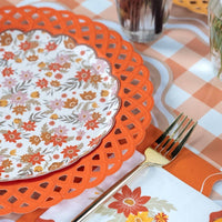 Styled fall table showing orange floral plates on an orange lattice charger with gold flatware and the orange scalloped napkins on a gingham surface.