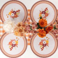 Overhead fall tablescape showing multiple floral placemats with floral plates, fresh flowers in vases, and gold accents on a gingham runner.