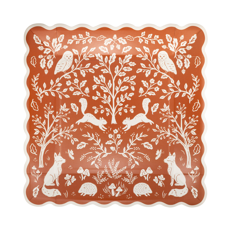 Fall woodland square paper plate in rust with a dense cream folk-art illustration of deer, birds, acorns, oak leaves, and mushrooms, cream wavy edge, overhead view on gray background.