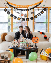 Two people sitting on a couch with Halloween decorations, including an orange & Black felt banner and pumpkin-themed items.
