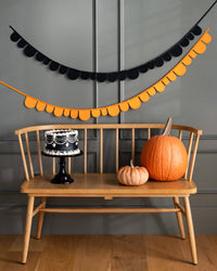 Both banners draped together across a mantel in a Halloween-decorated room with a cake, and pumpkins on a wooden bench.