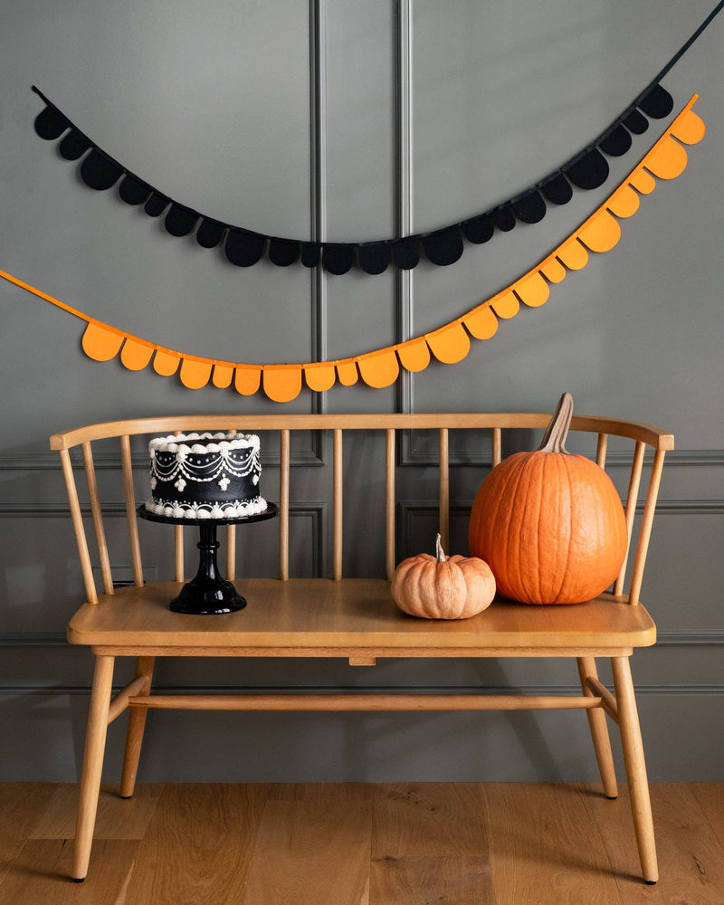 Both banners draped together across a mantel in a Halloween-decorated room with a cake, and pumpkins on a wooden bench.