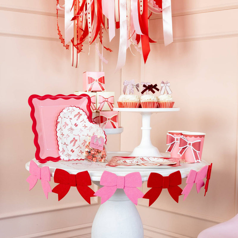 Valentine dessert table decorated with pink and red felt bow banner and coordinating tableware