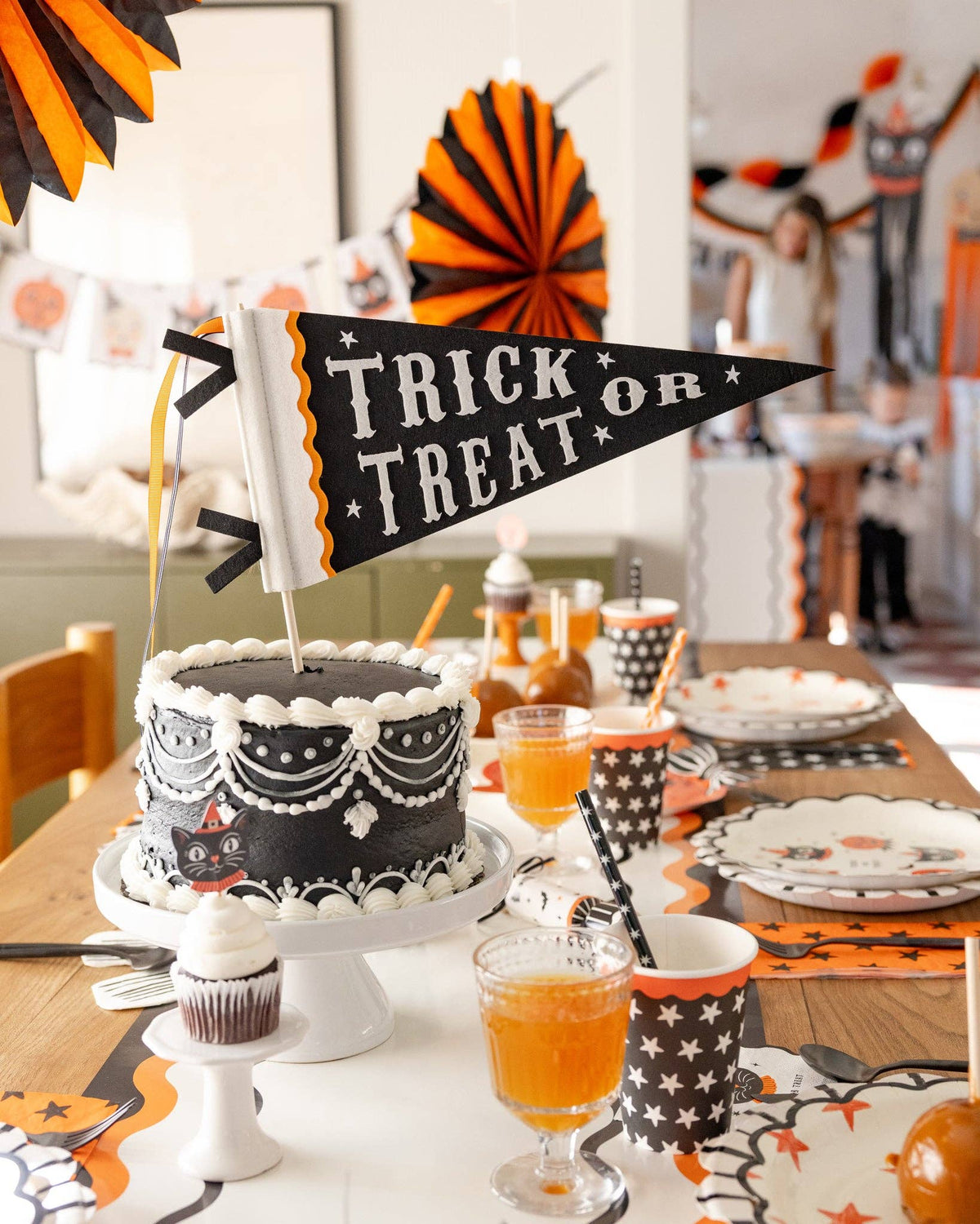 Halloween-themed table setting with a cake, drinks, and decorations with the Trick or Treat pennant.