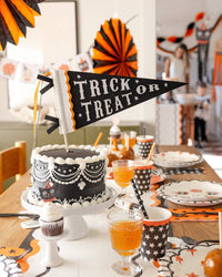 Halloween-themed table setting with a cake, drinks, and decorations with the Trick or Treat pennant.