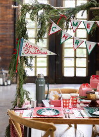 Rustic window room with the felt pennant flag, a Merry Christmas banner, and gingham cups on a table.