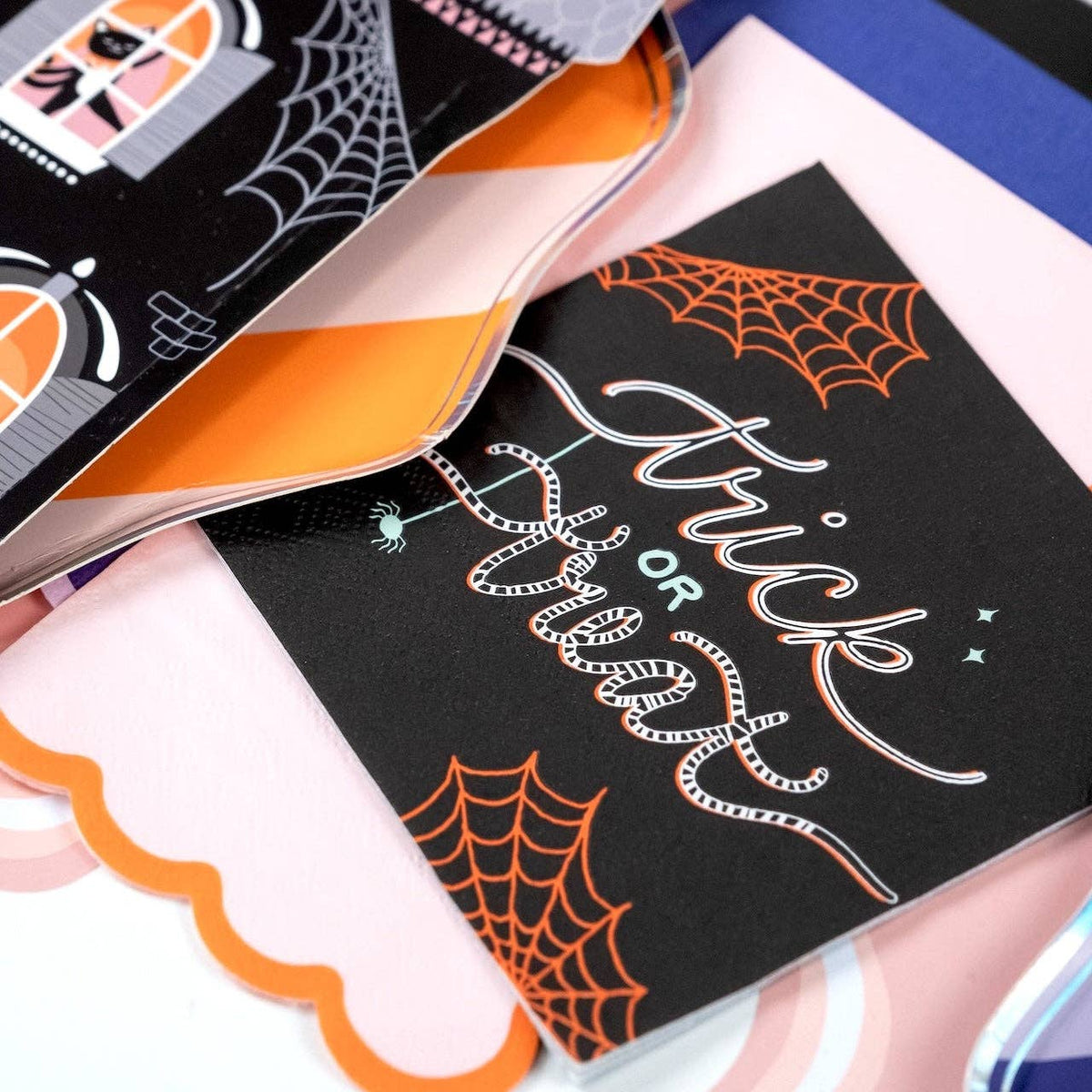 Styled feminine Halloween table showing the trick or treat napkin on a pink scalloped charger with an orange ribbon and spiderweb-detailed plate.