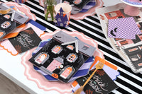 Overhead of a feminine Halloween table with multiple settings — trick or treat napkins, pink chargers, purple plates, and orange accents.