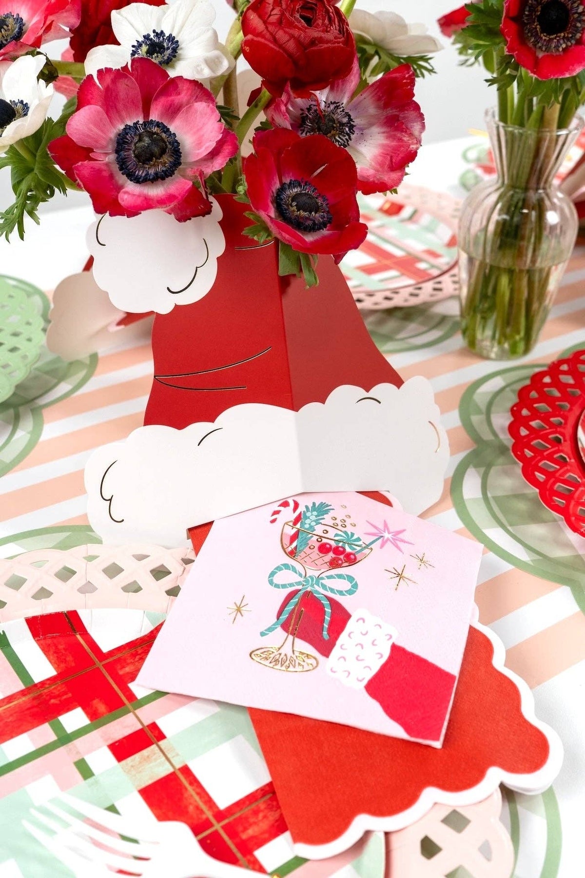 Wide festive holiday tablescape featuring red and green plaid plates, pink cocktail napkins, and red floral centerpieces.