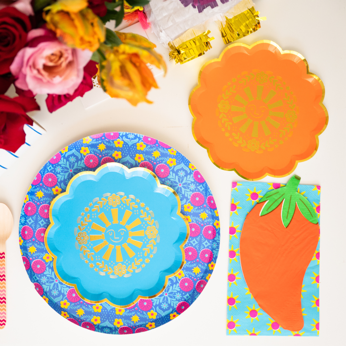 This photo shows a colorful taco-themed party table with sun plates, chili pepper napkins, flowers, and fiesta decorations.
