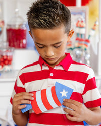 Boy in red and white striped polo holding a firecracker shaped paper napkin at a patriotic candy cart party