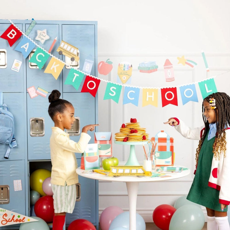 Kids celebrating first day of school with banner and themed table.