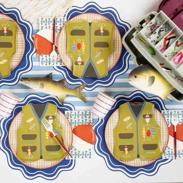 Fishing party tablescape with fish print napkins, vest shaped plates, bobber napkins, striped cups, and a tackle box.