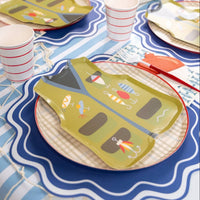 Fishing party place setting with a fish print napkin, vest shaped plate, plaid plate, striped cup, and tackle box.