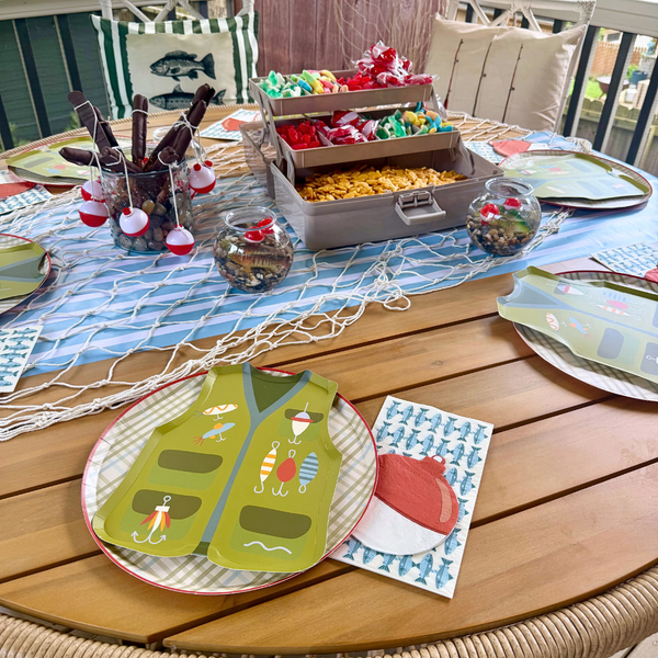 Fishing party tablescape with vest shaped paper plates, fish napkins, tackle box snack station, and nautical decorations