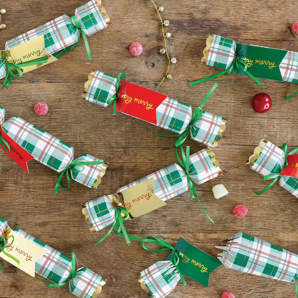 Overhead flat lay of several Christmas crackers scattered on a wooden table with greenery, ready for use as Christmas dinner favors.
