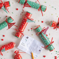 Overhead flat lay showing multiple holiday poppers scattered with the "Roll a Snowman" interactive dinner game card.