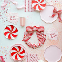 Flat lay showing multiple pink and red plates and party items scattered with confetti and striped ribbon.