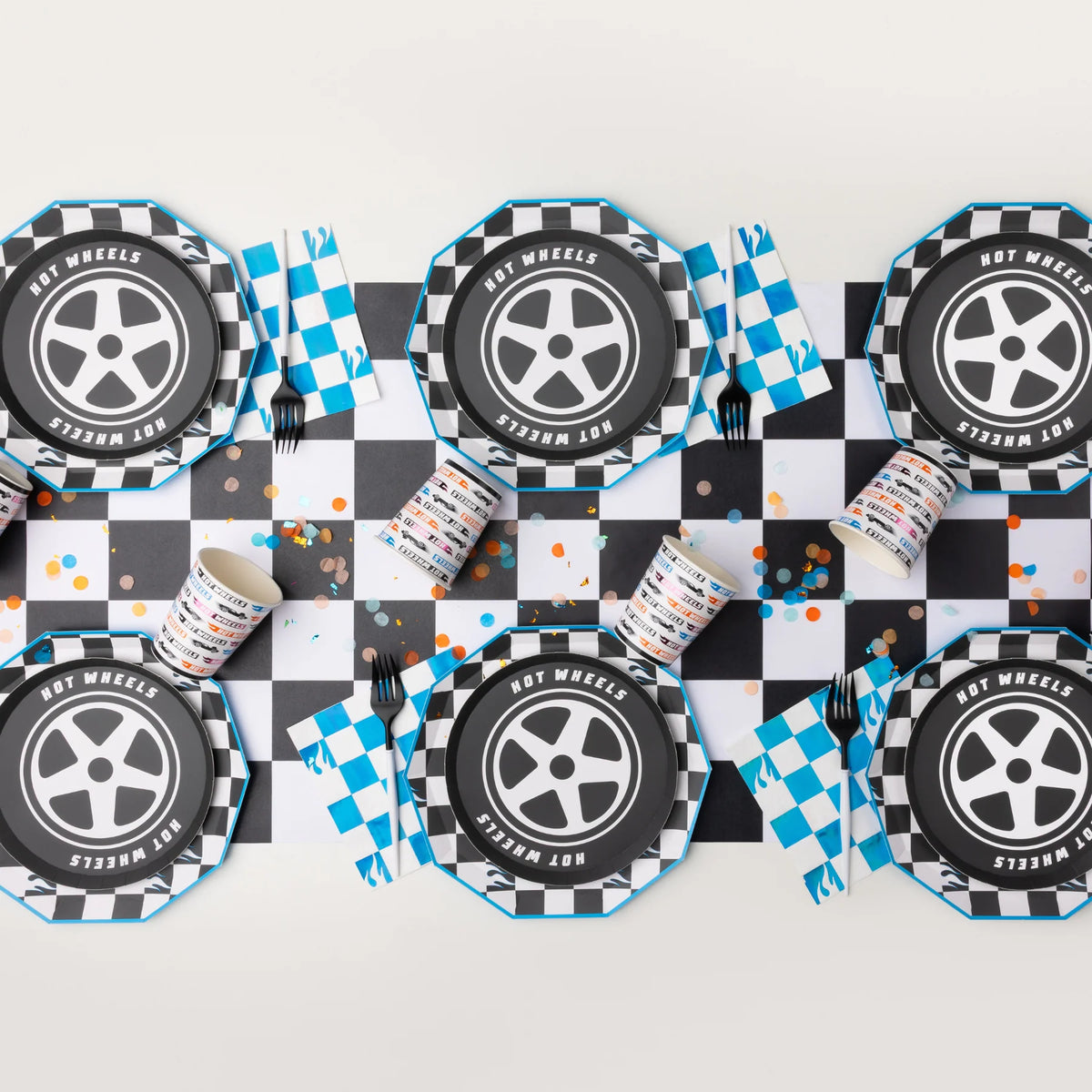 Overhead flat lay showing a large table display with checkered party supplies plates, cups, and race car napkins.