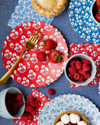 Overhead table setting with all four floral bamboo plates layered on blue tablecloth with strawberries, raspberries, pie, and gold forks