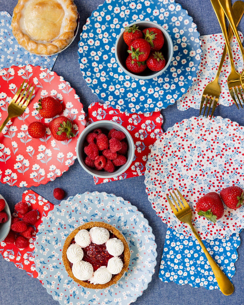 Overhead styled table with all four floral bamboo plate designs, fresh berries, pies with whipped cream, and gold forks on blue tablecloth