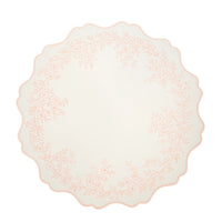 Single round blush pink placemat with a scalloped edge and floral border