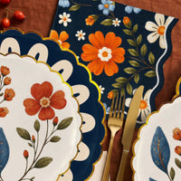 Folk floral napkin in navy with gold flatware and gold scalloped plates on rust linen
