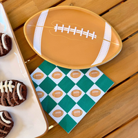 A brown, football-shaped party plate resting on a green and white checkered napkin decorated with mini footballs.