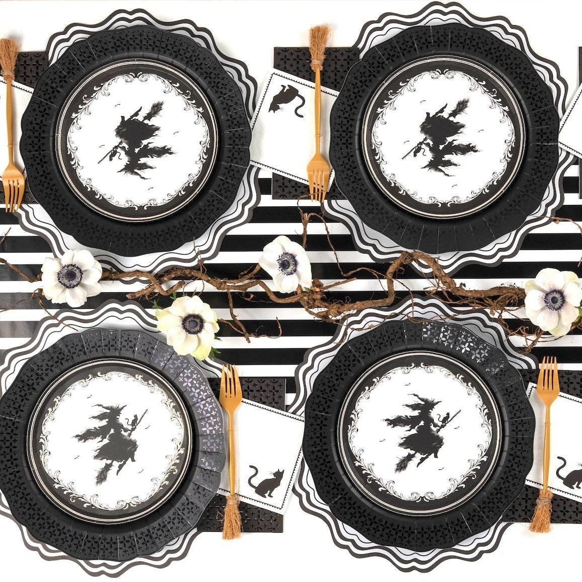 Overhead shot of four symmetrical Halloween place settings featuring witch plates layered on black die-cut chargers over a striped runner.