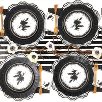 Overhead shot of four symmetrical Halloween place settings featuring witch plates layered on black die-cut chargers over a striped runner.
